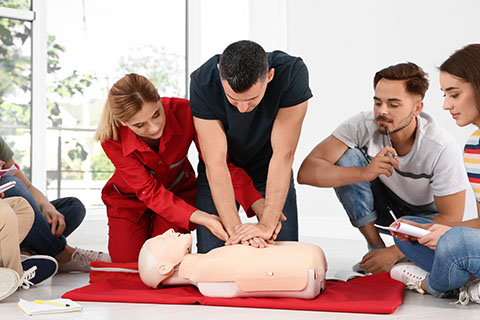 image of Group of people with instructor practicing CPR on mannequin at first aid class indoors