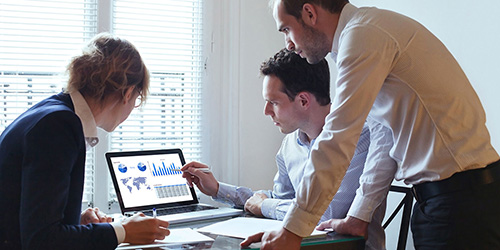 three office staff looking at graphs on a laptop